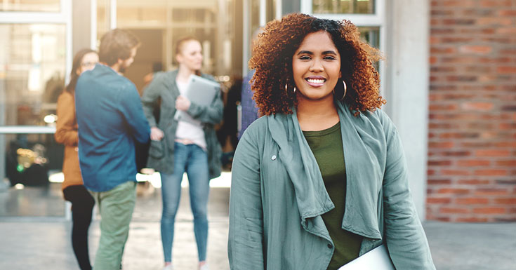 Portrait of a happy female student holding a laptop outdoors on campus