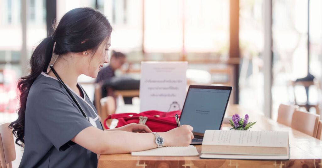 nursing student working online with a laptop sitting in campus library